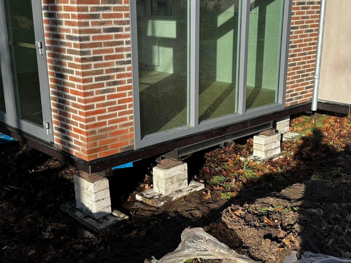 Bakstenen hoek van een woning op drie stapels bielzen in de herfstzon